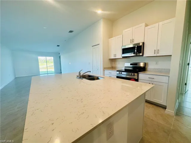 Kitchen featuring white cabinetry, stainless steel appliances, light stone countertops, lofted ceiling, and a kitchen island with sink