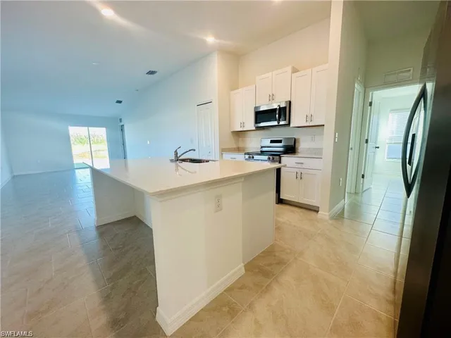 Kitchen featuring white cabinetry, stainless steel appliances, an island with sink, vaulted ceiling, and light tile patterned floors