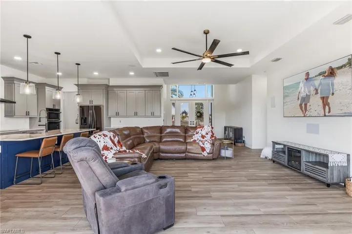 Living area featuring a raised ceiling, ceiling fan, light wood-type flooring, recessed lighting, and french doors