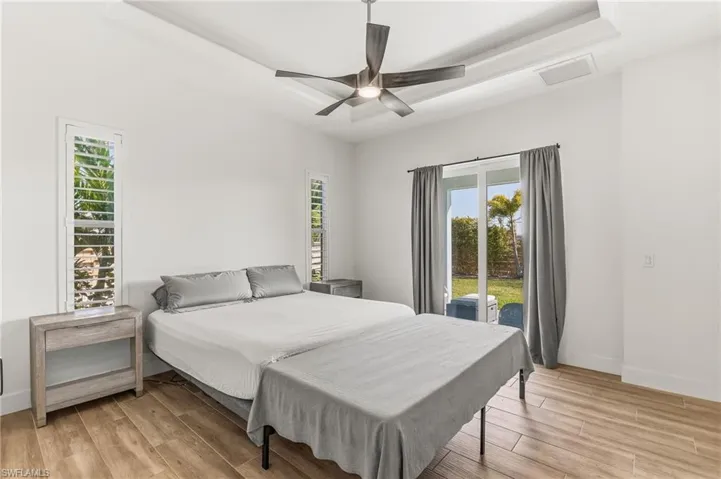 Bedroom with light wood-style flooring, access to outside, a tray ceiling, and ceiling fan