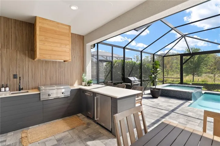 View of patio / terrace featuring glass enclosure, a grill, a sink, and an outdoor kitchen