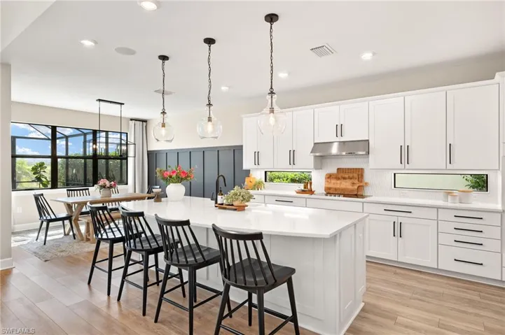 Kitchen featuring light countertops, tasteful backsplash, a center island with sink, under cabinet range hood, and visible vents