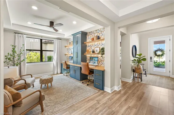 Office space featuring built in study area, light wood-style floors, ceiling fan, and a raised ceiling