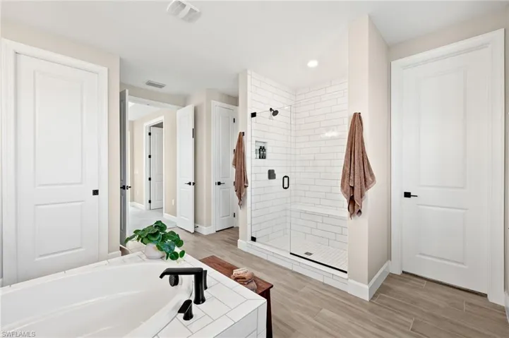 Bathroom with a garden tub, a shower stall, wood finish floors, baseboards, and visible vents