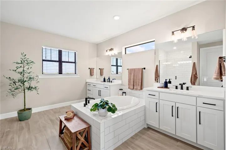 Full bath with a stall shower, a sink, two vanities, a garden tub, and baseboards