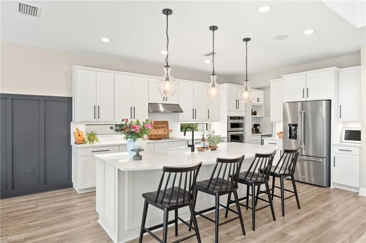 Kitchen featuring a kitchen island with sink, light countertops, under cabinet range hood, and stainless steel appliances