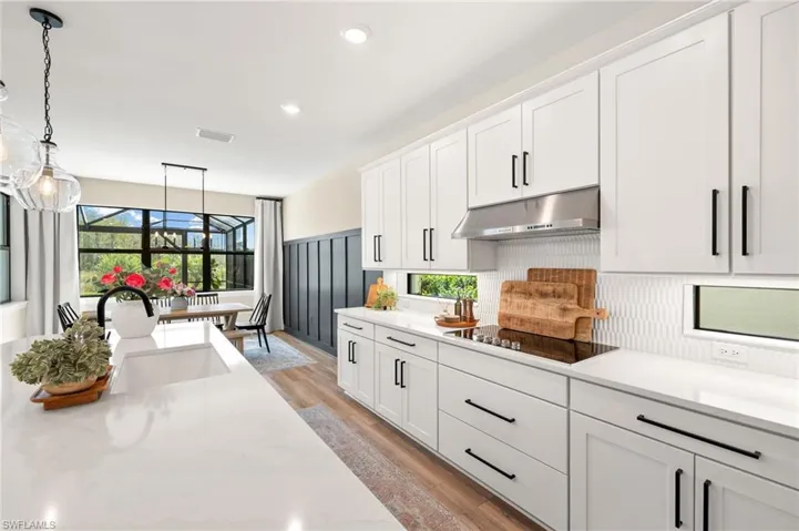 Kitchen featuring black electric cooktop, under cabinet range hood, a sink, visible vents, and white cabinets
