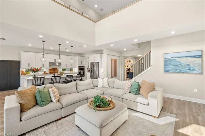 Living room featuring stairs, a high ceiling, light wood-style flooring, baseboards, and visible vents