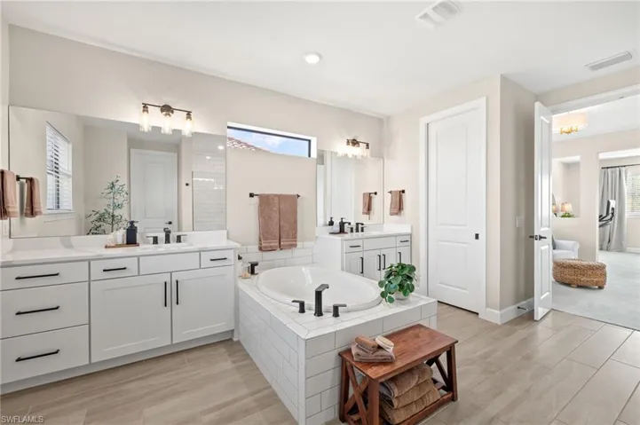 Full bath with a sink, two vanities, a garden tub, wood finished floors, and visible vents