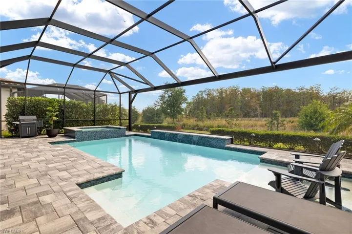 View of swimming pool featuring glass enclosure, grilling area, a pool with connected hot tub, and a patio area