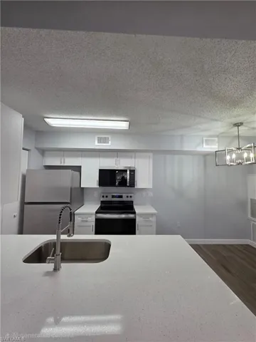 Kitchen with stainless steel appliances, white cabinets, dark wood-style floors, a textured ceiling, and decorative light fixtures
