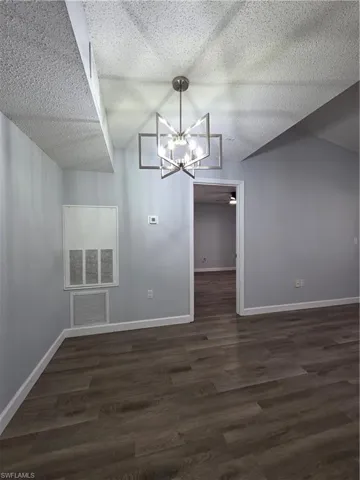 Unfurnished dining area with suspended lighting, dark wood-type flooring, and a textured ceiling