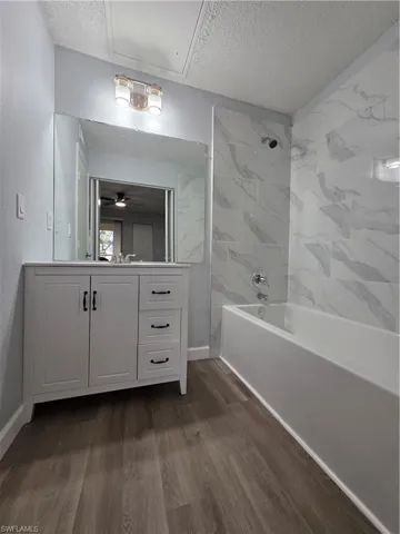 Full bath with  shower combination, vanity, a textured ceiling, dark wood-style flooring, and ceiling fan