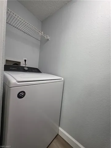 Laundry area featuring washer / clothes dryer, a textured wall, a textured ceiling, and wood finished floors