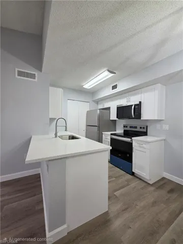 Kitchen featuring stainless steel appliances, white cabinetry, dark wood-style flooring, a textured ceiling, and a peninsula
