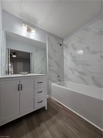 Bathroom with tub / shower combination, vanity, dark wood-style flooring, a textured ceiling, and ceiling fan