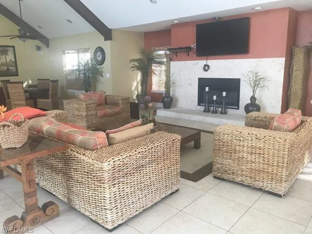 Tiled living area featuring a ceiling fan, healthy amount of natural light, a fireplace, and vaulted ceiling with beams