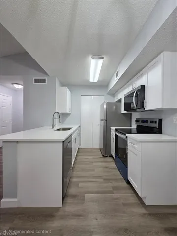 Kitchen with stainless steel appliances, a textured ceiling, white cabinets, light wood finished floors, and a peninsula