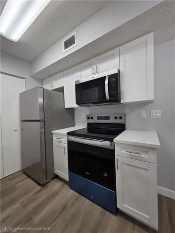 Kitchen featuring stainless steel appliances, white cabinetry, dark wood-type flooring, and a textured ceiling