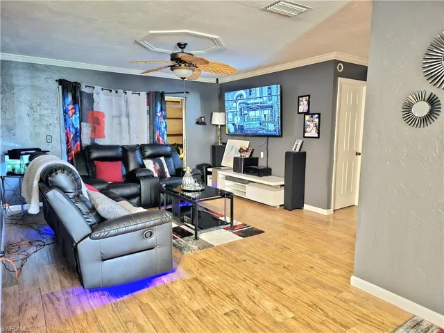 Living room featuring wood-type flooring, ornamental molding, and ceiling fan