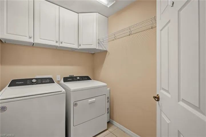 Laundry room featuring washer and dryer, light tile patterned flooring, and cabinets