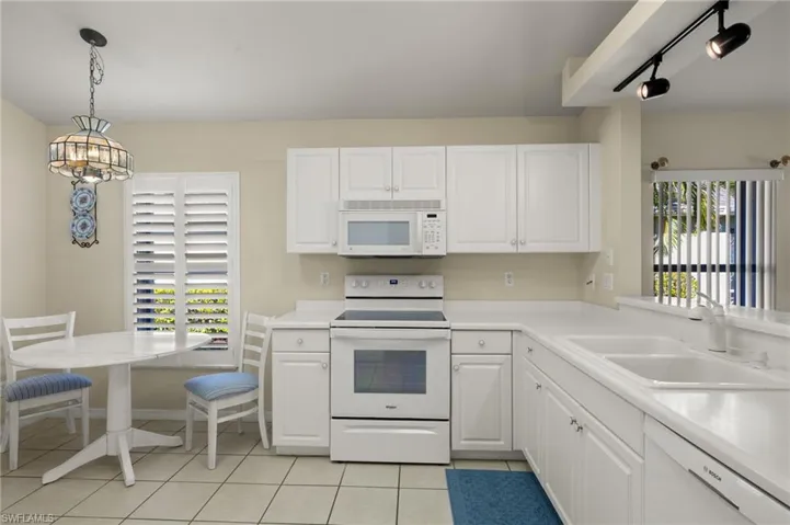 Kitchen featuring sink, white cabinetry, white appliances, light tile patterned flooring, and hanging light fixtures