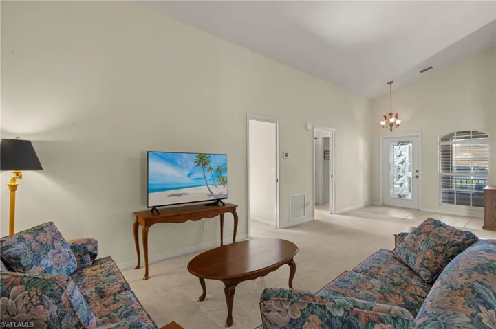 Carpeted living room with high vaulted ceiling and a notable chandelier