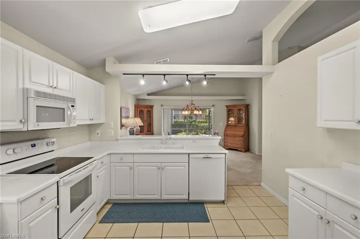 Kitchen with white appliances, light tile patterned floors, sink, white cabinetry, and lofted ceiling