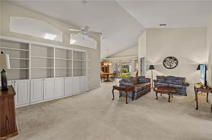 Carpeted living room with ceiling fan with notable chandelier and high vaulted ceiling