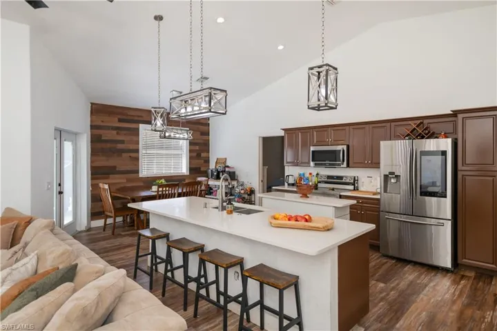 Kitchen with wood walls, stainless steel appliances, a kitchen breakfast bar, lofted ceiling, and dark wood finished floors