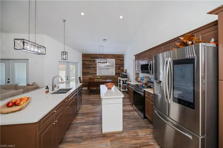 Two tone kitchen with stainless steel appliances, a center island with sink, wooden walls, french doors, and open floor plan