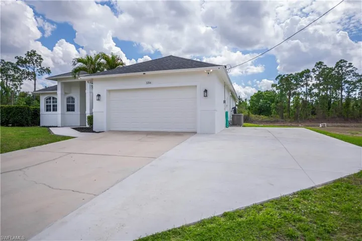 View of front of house featuring stucco siding, an attached garage, concrete driveway, and a front yard