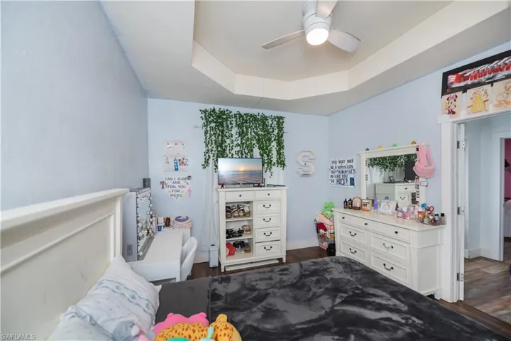 Bedroom with dark wood-style floors, a raised ceiling, and a ceiling fan