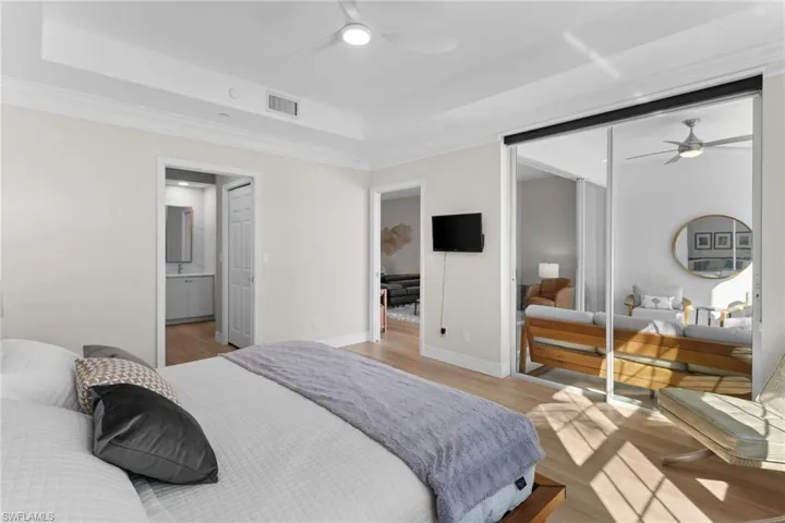 Bedroom with a closet, light wood-type flooring, ceiling fan, crown molding, and a tray ceiling