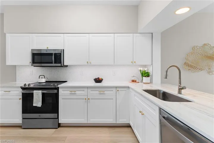 Kitchen with stainless steel appliances, white cabinetry, light stone counters, and backsplash