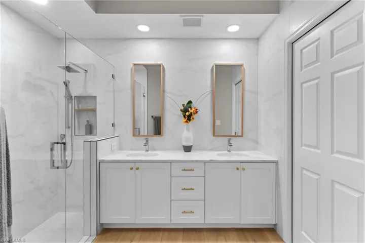 Full bathroom with double vanity, a marble finish shower, recessed lighting, tile walls, and light wood-type flooring