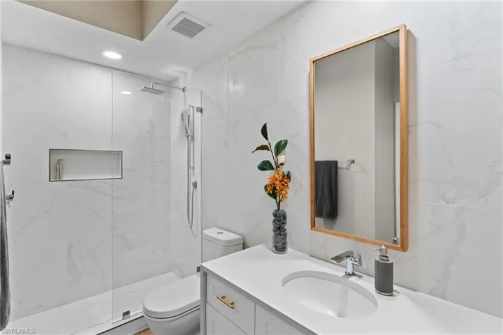 Bathroom featuring a marble finish shower, vanity, and tile walls