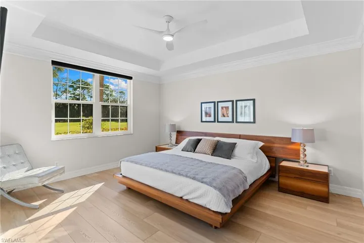 Bedroom with wood finished floors, ceiling fan, a raised ceiling, and crown molding