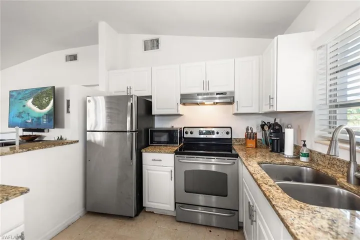 Kitchen featuring stainless steel appliances, lofted ceiling, white cabinetry, and light stone counters
