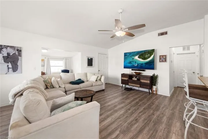 Living room with dark wood-type flooring, a ceiling fan, and vaulted ceiling