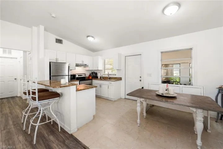 Kitchen featuring a breakfast bar area, stainless steel appliances, white cabinets, vaulted ceiling, and dark stone countertops