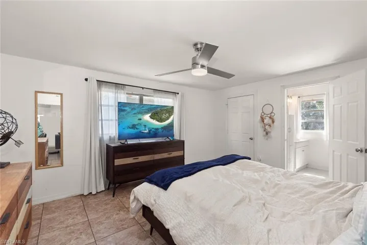 Bedroom featuring ceiling fan, light tile patterned floors, and ensuite bathroom