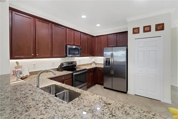 Kitchen with light stone countertops, sink, stainless steel appliances, light tile patterned floors, and ornamental molding