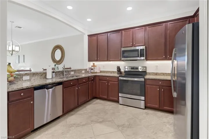 Kitchen with pendant lighting, light stone countertops, sink, and appliances with stainless steel finishes