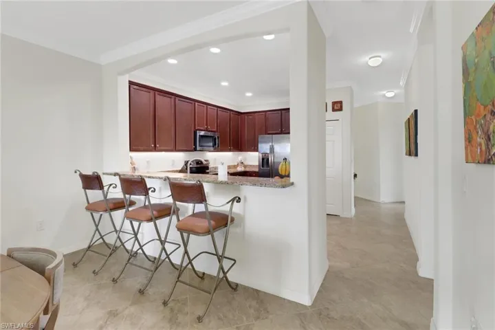 Kitchen featuring light stone countertops, appliances with stainless steel finishes, kitchen peninsula, a breakfast bar, and crown molding