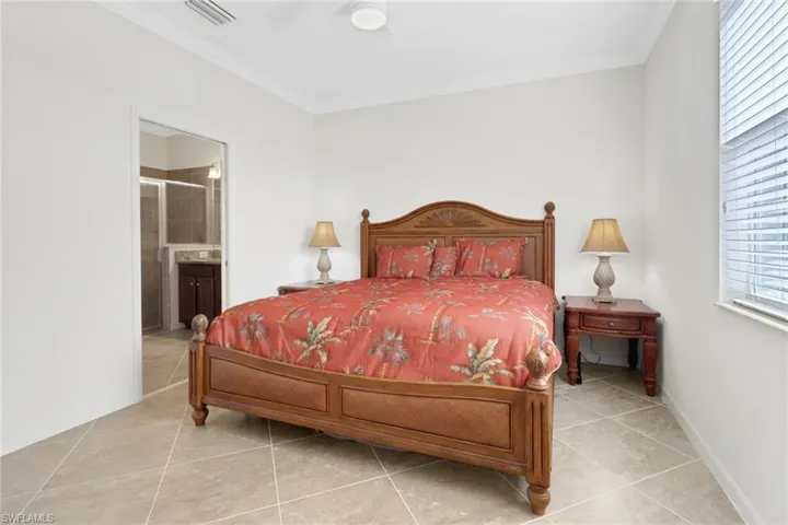 Tiled bedroom with ensuite bathroom, ceiling fan, and ornamental molding