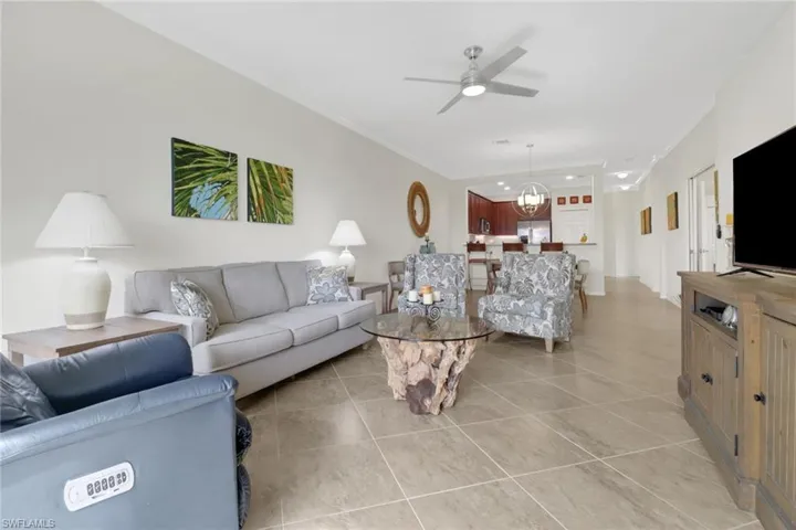 Living room featuring ceiling fan with notable chandelier, light tile patterned flooring, and ornamental molding