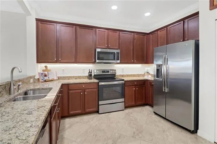 Kitchen with light stone counters, sink, ornamental molding, and stainless steel appliances