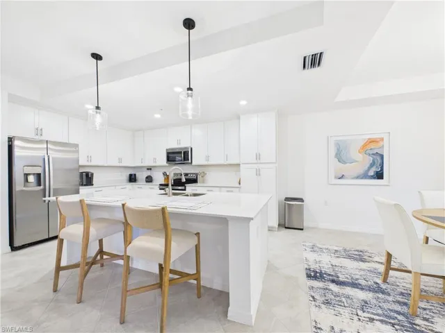 Kitchen with stainless steel appliances, light countertops, a breakfast bar area, a kitchen island with sink, and white cabinets
