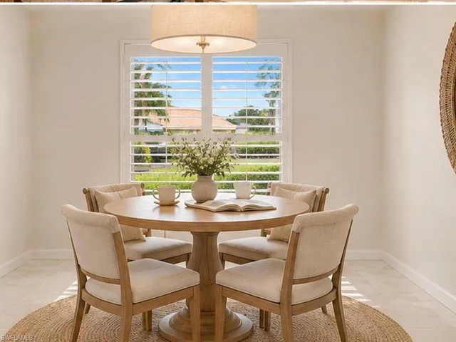 Neutral-toned interior space featuring a drum pendant light fixture, window with plantation shutters, and light-toned tile flooring